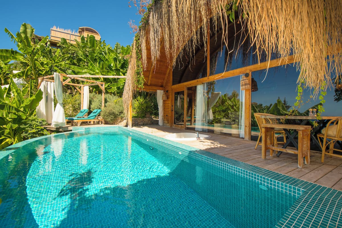A swimming pool with clear blue water, surrounded by lush greenery and a wooden deck.
