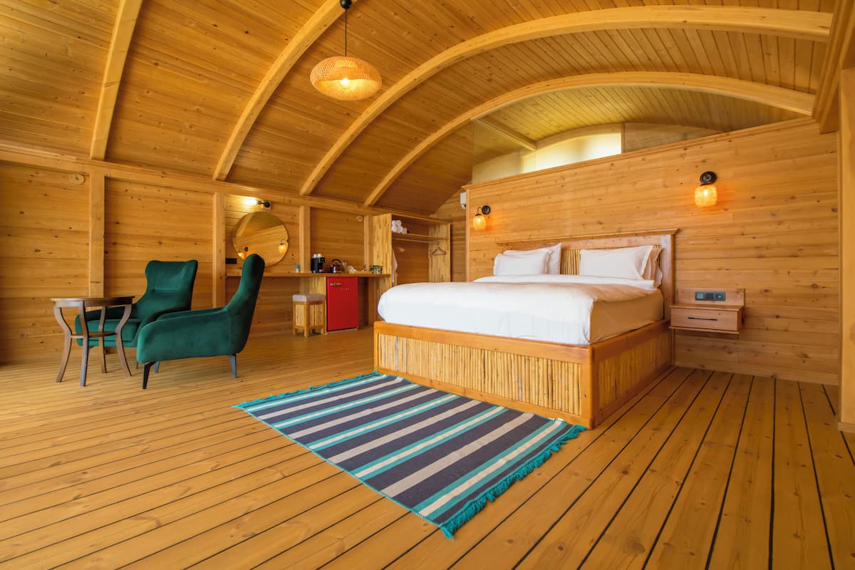 A wooden cabin bedroom with a bed, a chair, a small table, and a nightstand.