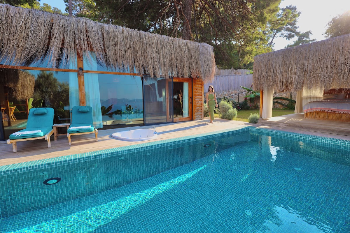 A modern villa with a swimming pool, lounge chairs, and a thatched roof structure.