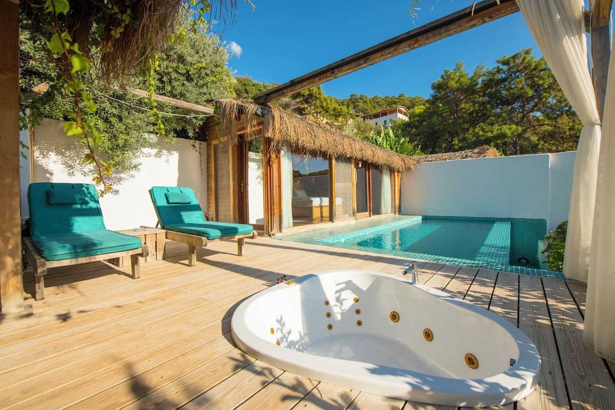 A wooden deck with a hot tub, two green lounge chairs, and a pool.