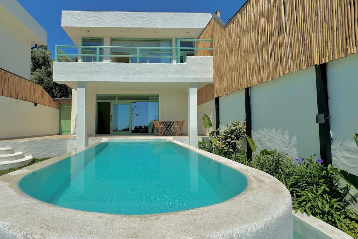 A modern two-story house with a swimming pool in the foreground.