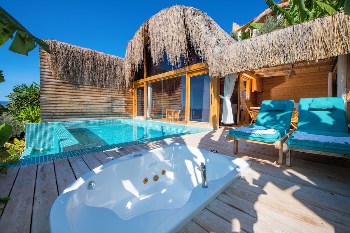 A wooden deck with a hot tub, lounge chairs, and a pool area with a thatched roof.