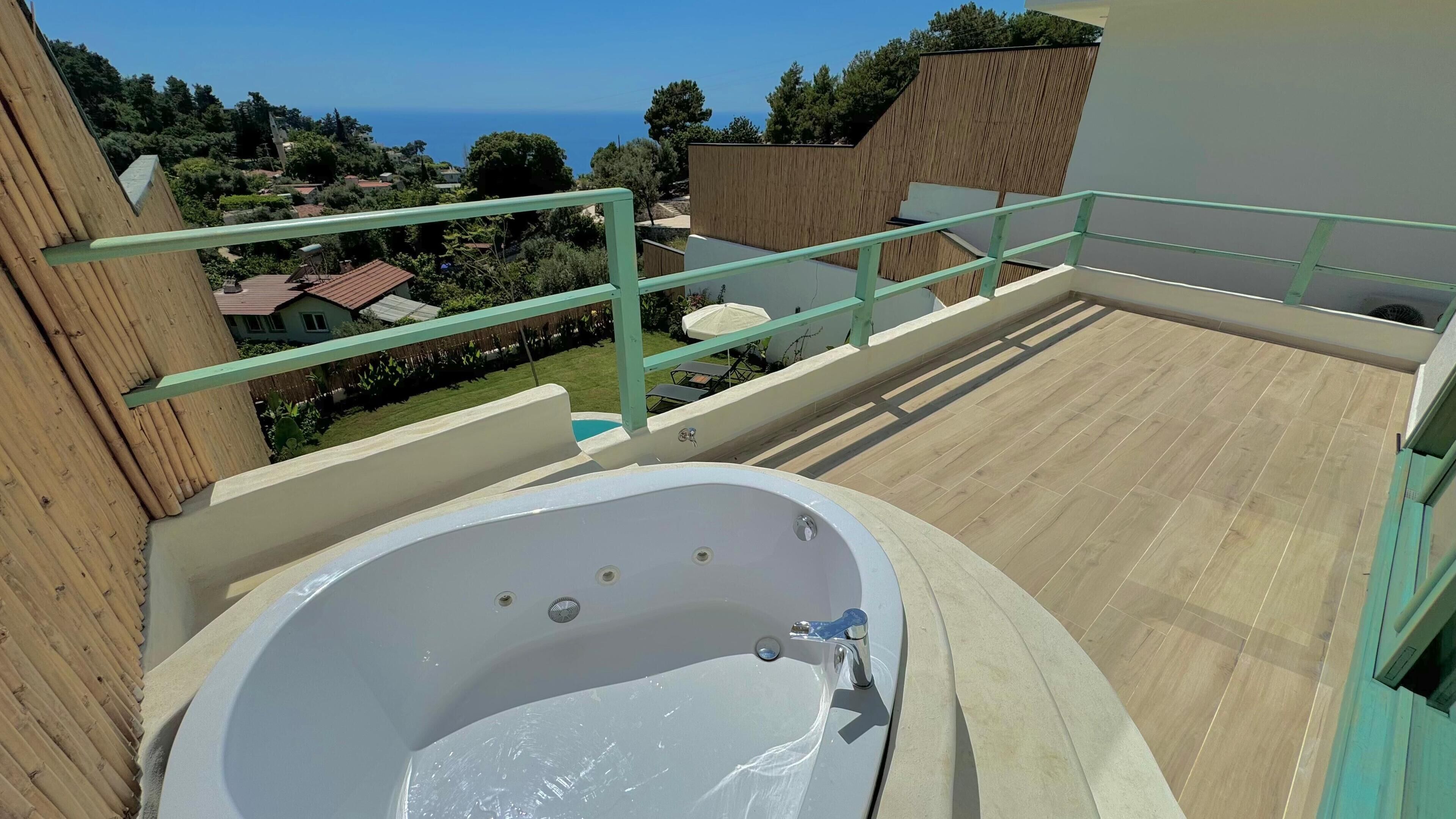 A rooftop terrace with a hot tub, wooden railings, and a view of the sea and houses.