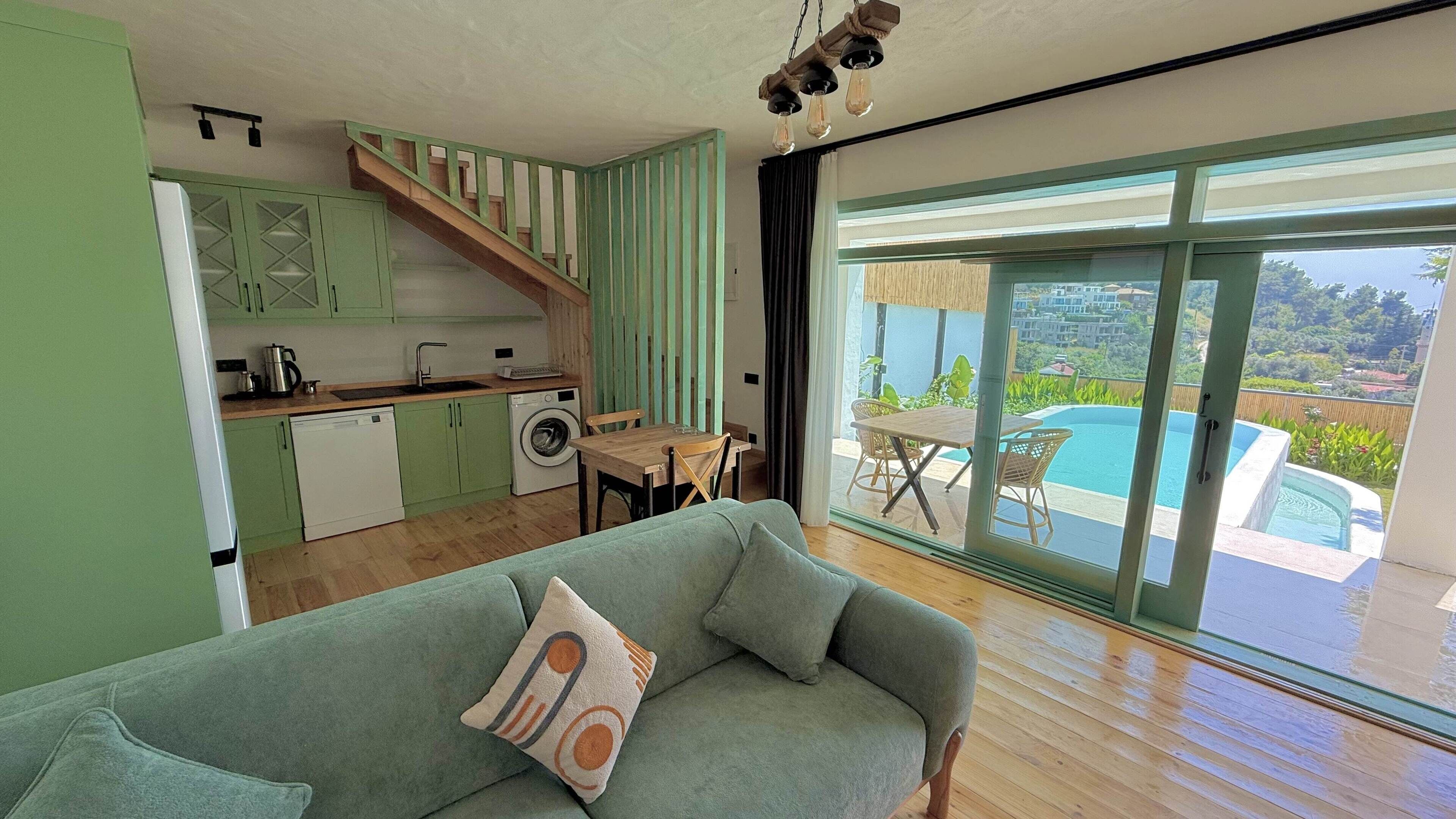 A modern kitchen with green cabinets, a wooden staircase, a dining area with a table and chairs, and a large sliding glass door leading to a pool.