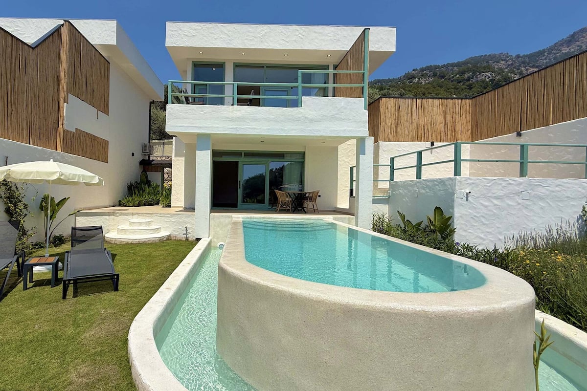 A modern two-story house with a swimming pool, outdoor seating, and a view of the surrounding landscape.