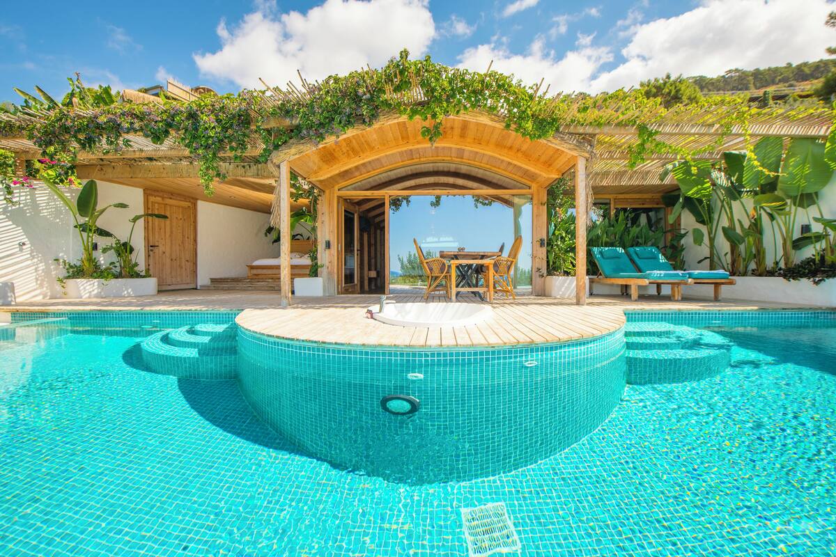 A pool area with a wooden deck, lounge chairs, and a covered seating area.