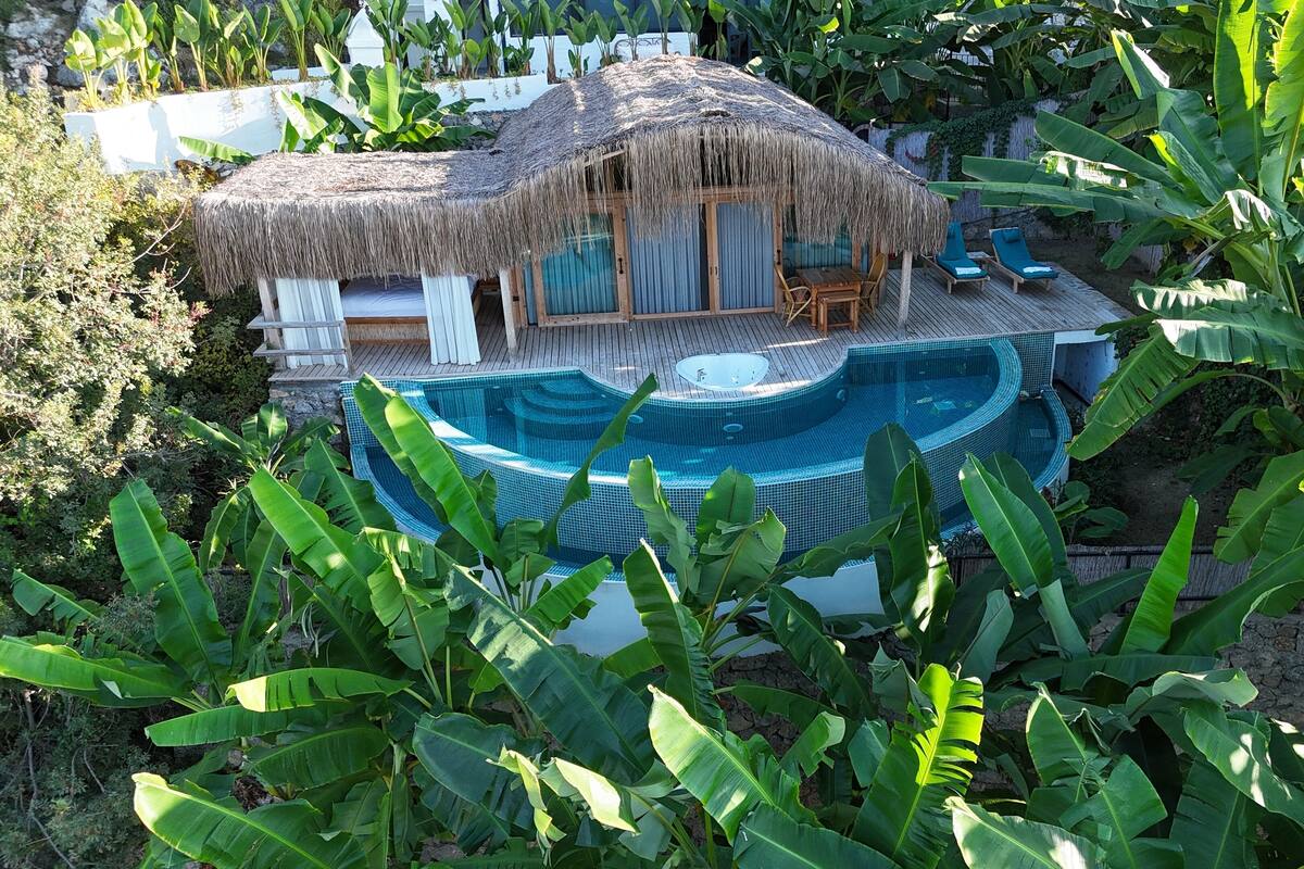 A poolside area with a hot tub, lounge chairs, and a thatched-roof structure.