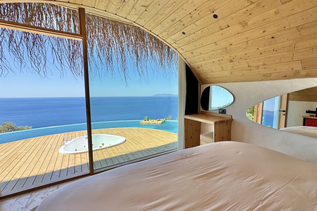 A bedroom with a large bed, a wooden desk, and a view of the ocean.