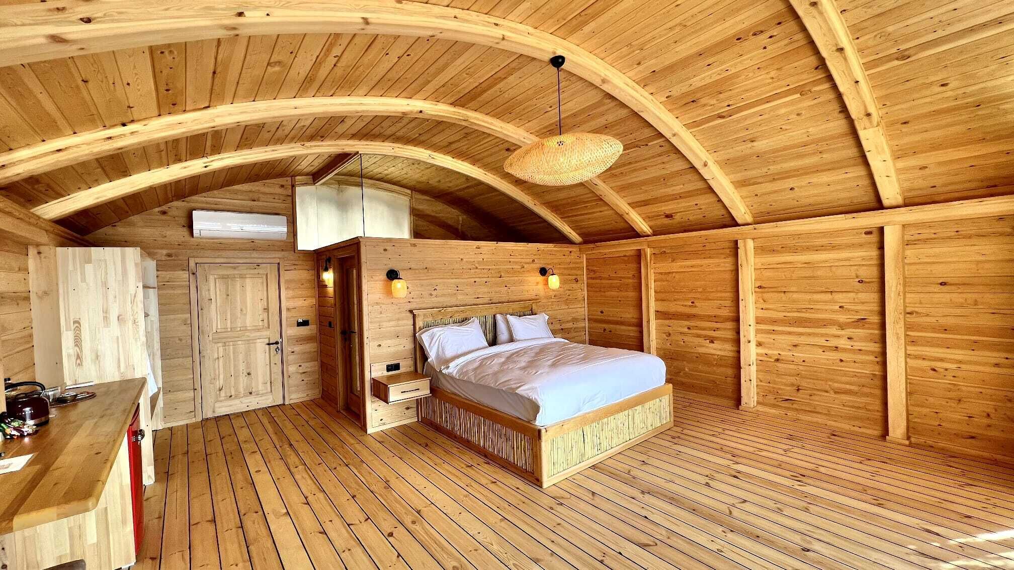 Ett sovrum i en stuga med träpanel, inrett med en säng, sängbord och en hängande lampa.