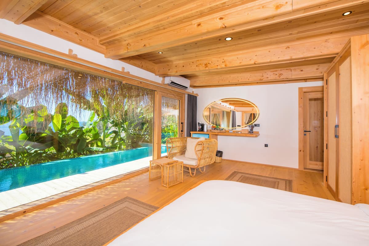A wooden room with a large window, a bed, a chair, and a small table.