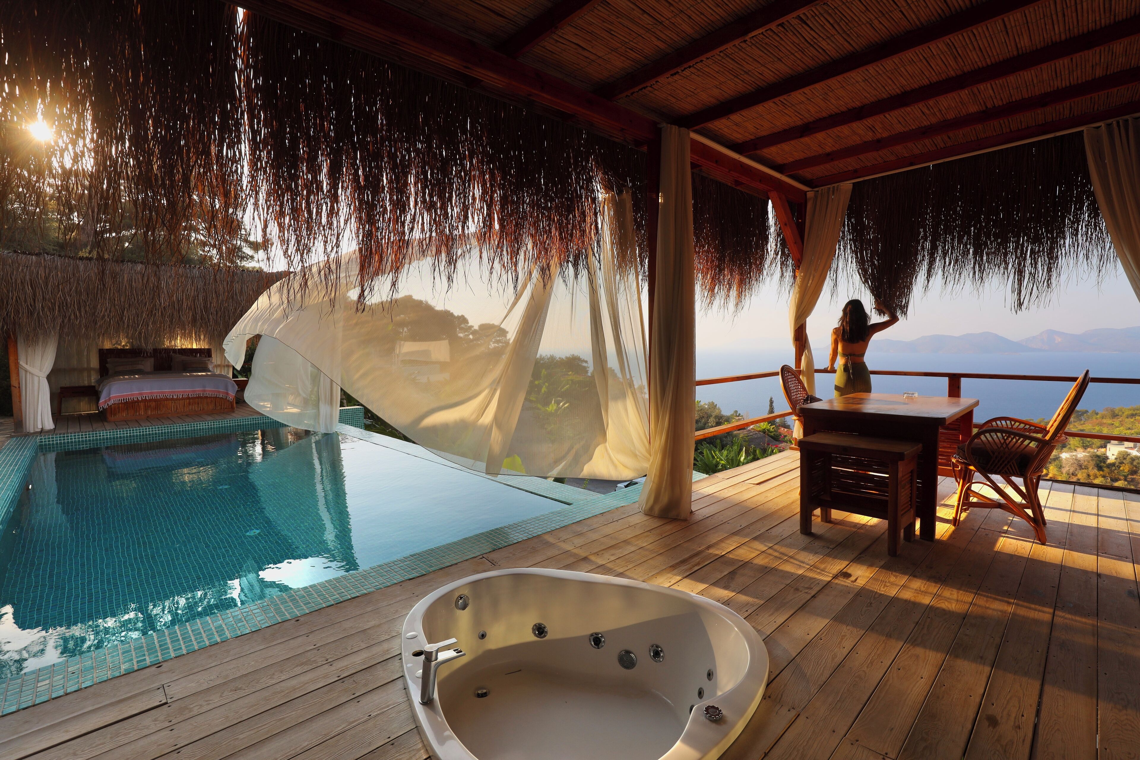 A wooden deck with a hot tub, a pool, and a table with chairs.