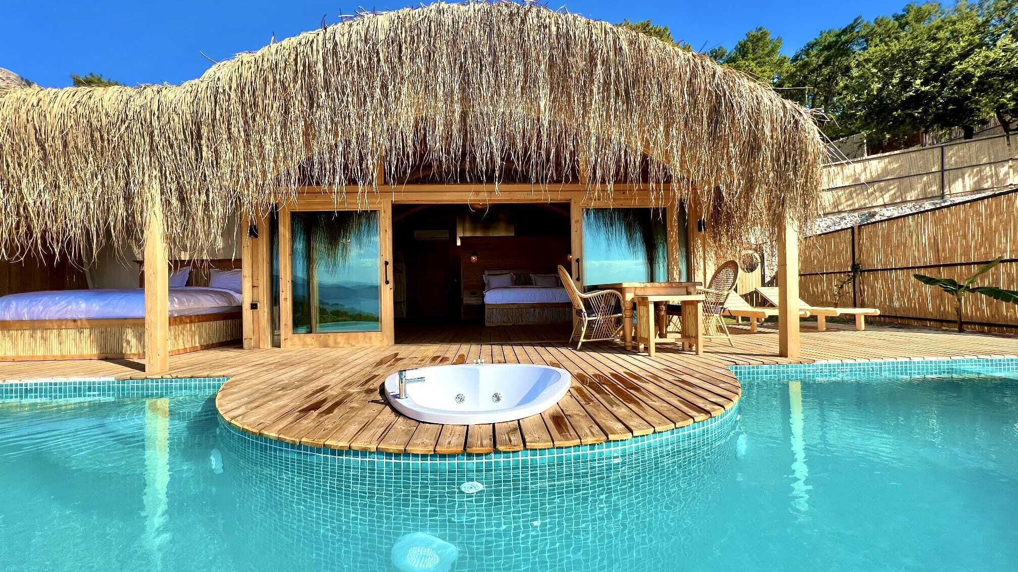 Estructura con techo de paja, piscina, bañera de hidromasaje, terraza de madera y vistas del paisaje.