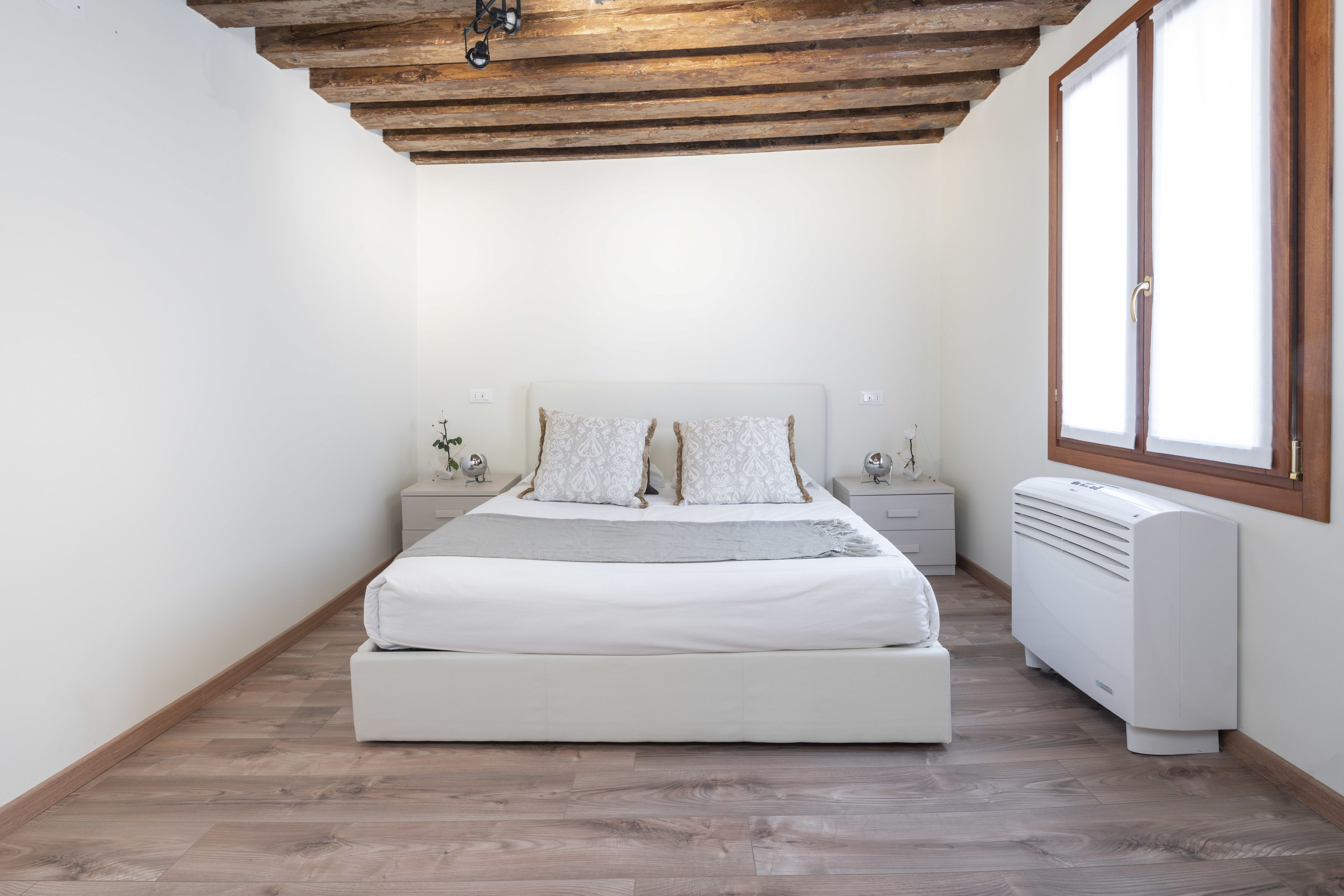 A bedroom with a wooden ceiling, a bed with white bedding, bedside tables, and a radiator.