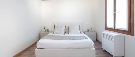 A bedroom with a wooden ceiling, a bed with white bedding, bedside tables, and a radiator.