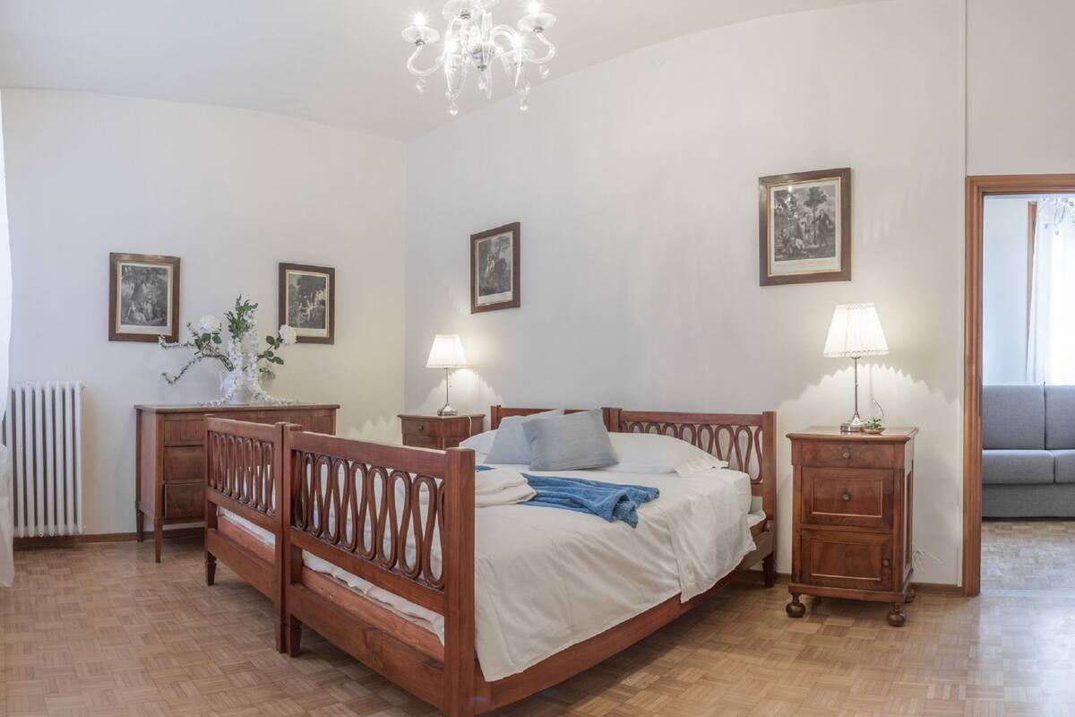 A bedroom with a wooden bed, two bedside tables, a radiator, and a chandelier.