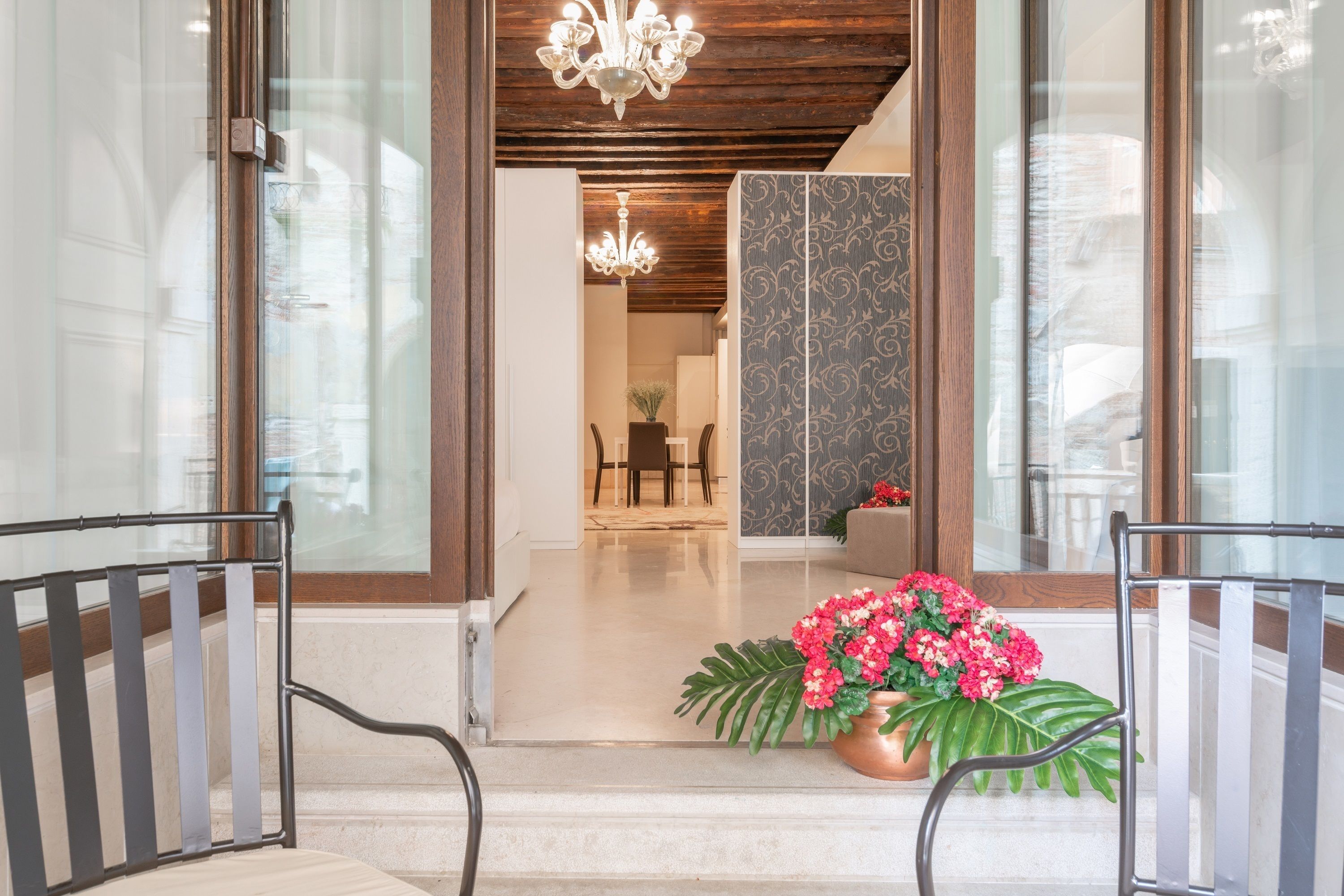 A hotel entrance with a chandelier, a dining area in the background, and a potted plant with pink flowers.