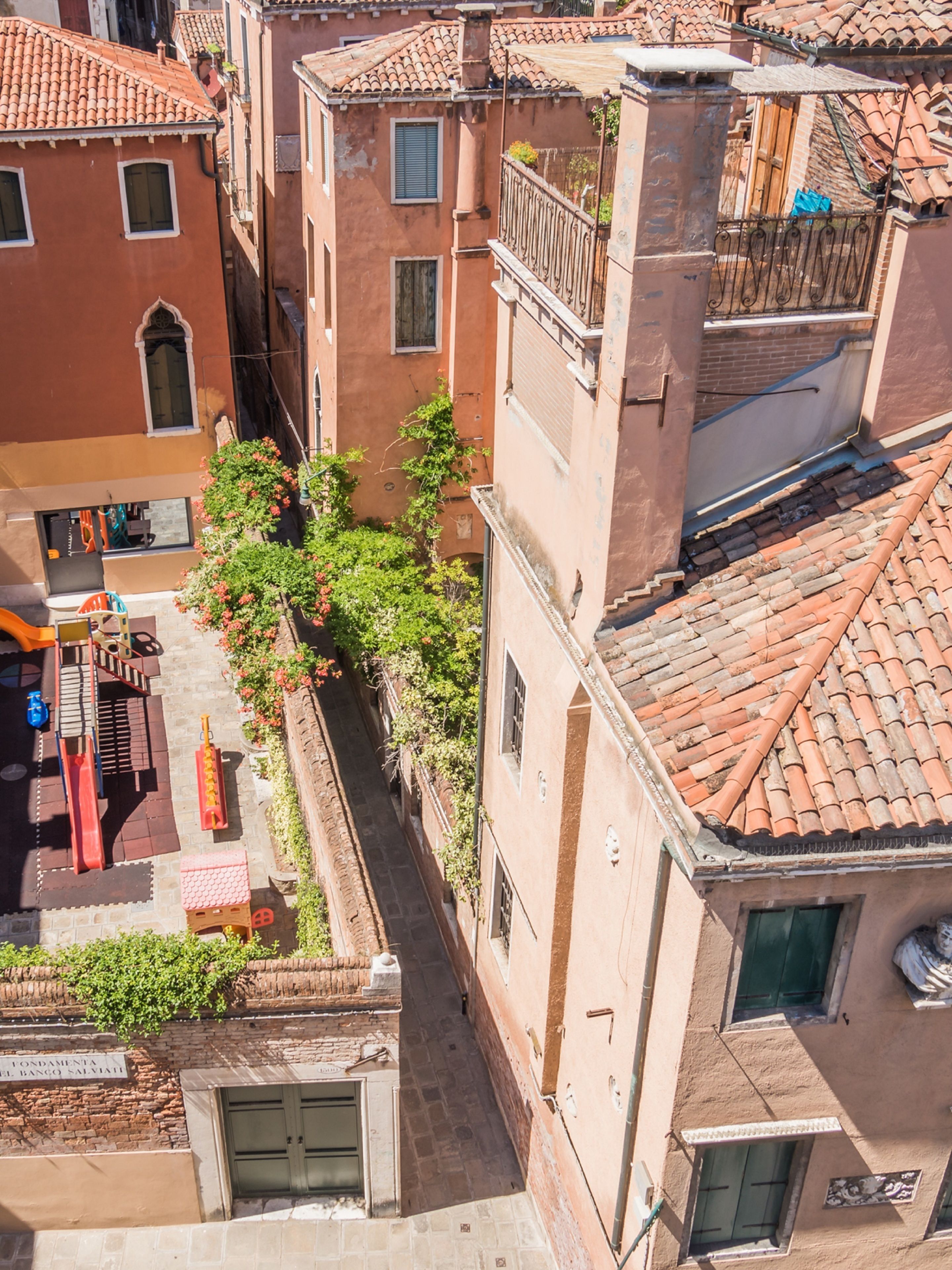 A narrow alley between buildings with a playground and a sign for "Fondamenta del Banco Salviati".