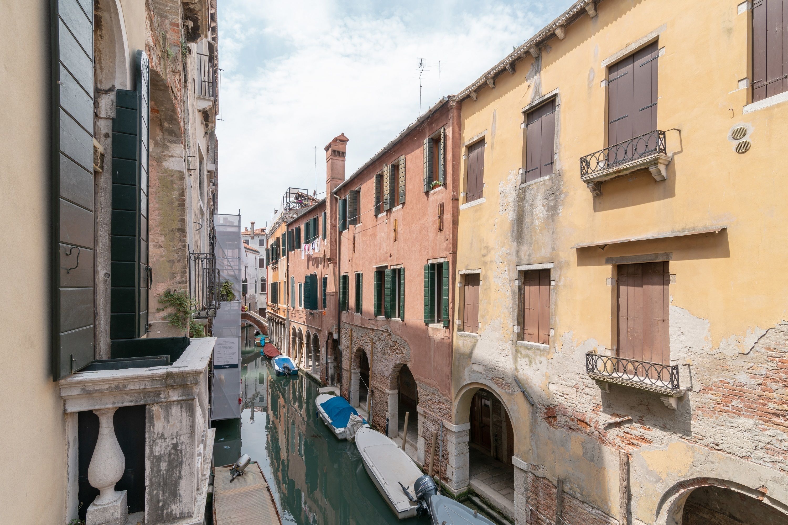 A narrow canal with buildings on either side, featuring arched doorways and balconies.