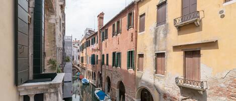 A narrow canal with buildings on either side, featuring arched doorways and balconies.