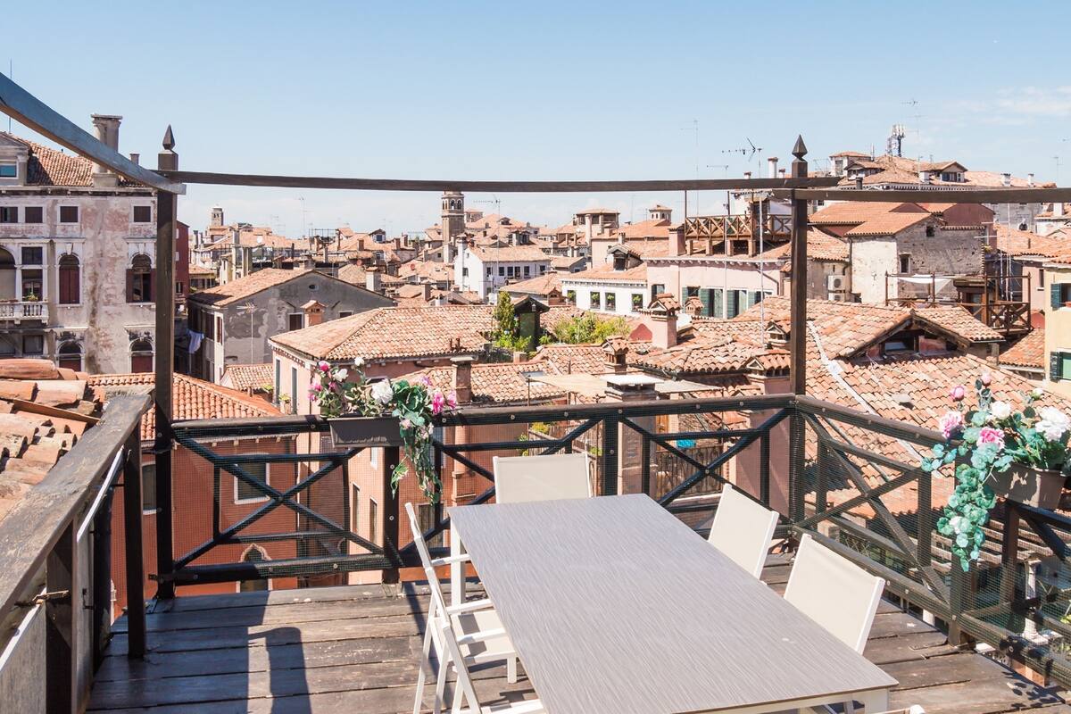 A terrace with a table and chairs, overlooking a densely packed urban area with traditional buildings and a clear sky.