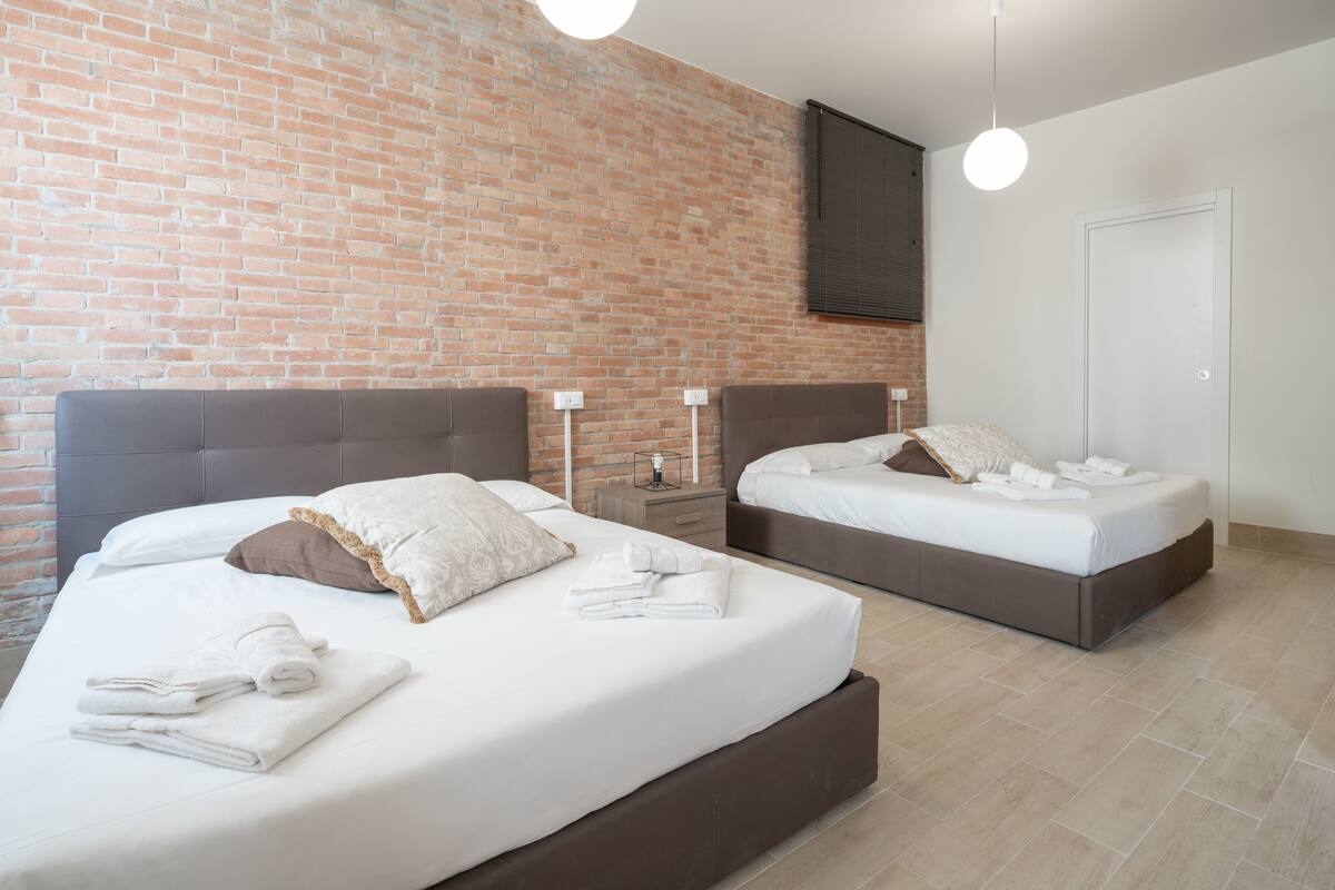 A hotel room with two beds, a brick wall, a wooden floor, and a door.