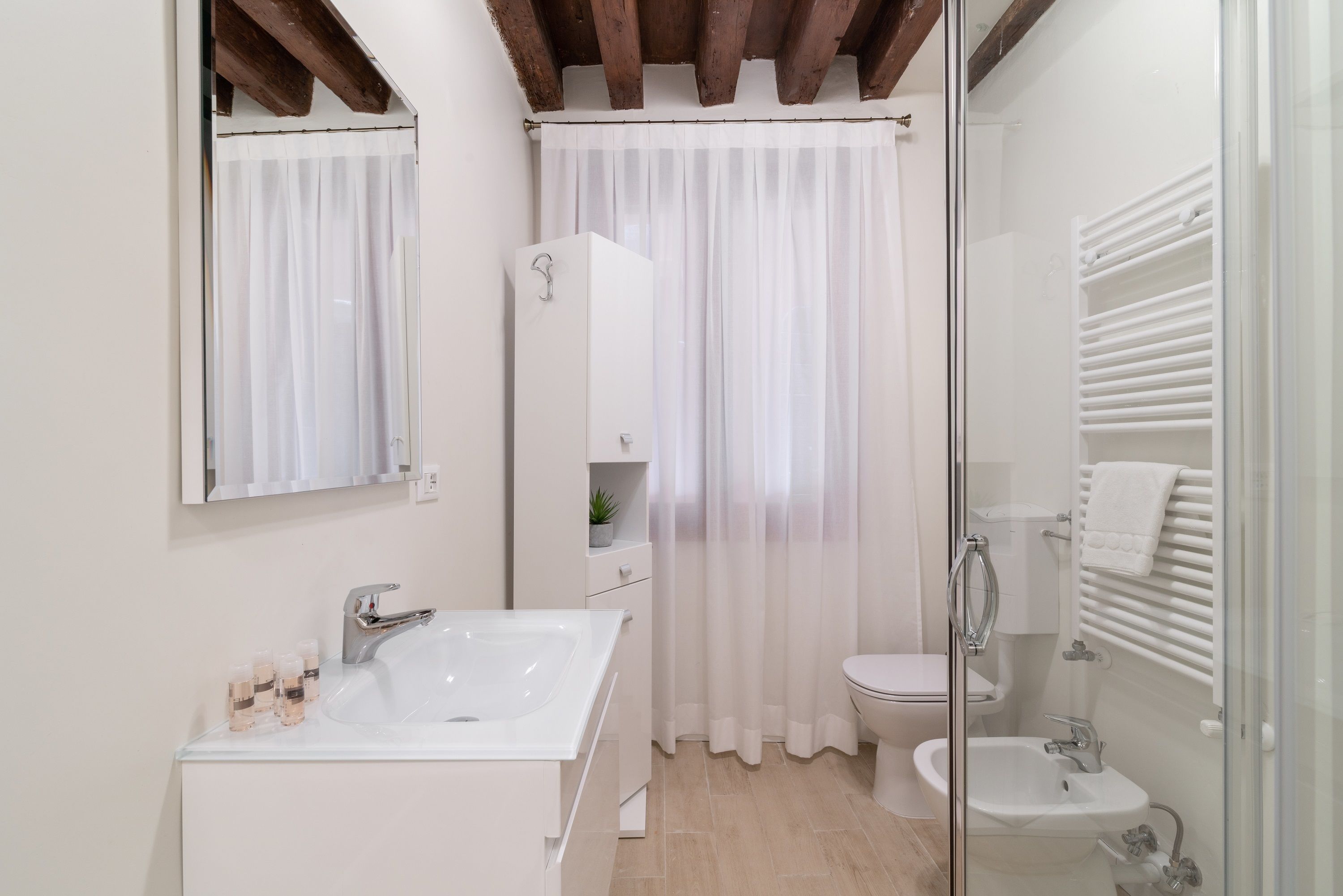 A modern bathroom with a white sink, toilet, and bidet, a glass shower enclosure, and a mirror above the sink.