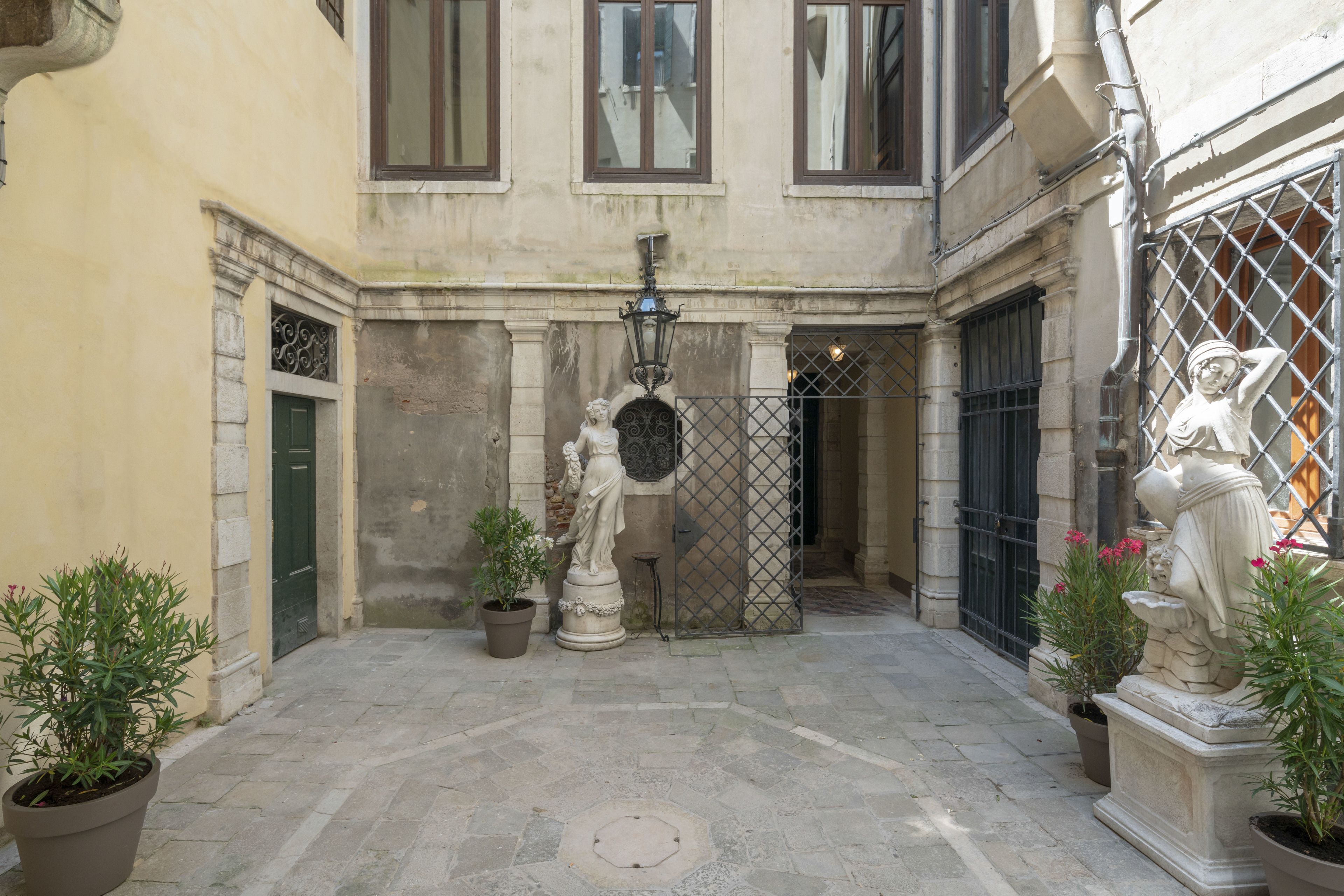 A courtyard with a statue, potted plants, and a gate.
