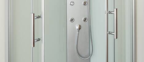 Box doccia in vetro con soffione a mano, pannello comandi a parete e porta in vetro.