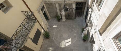 A narrow courtyard with a tiled floor, a statue, and a metal railing.