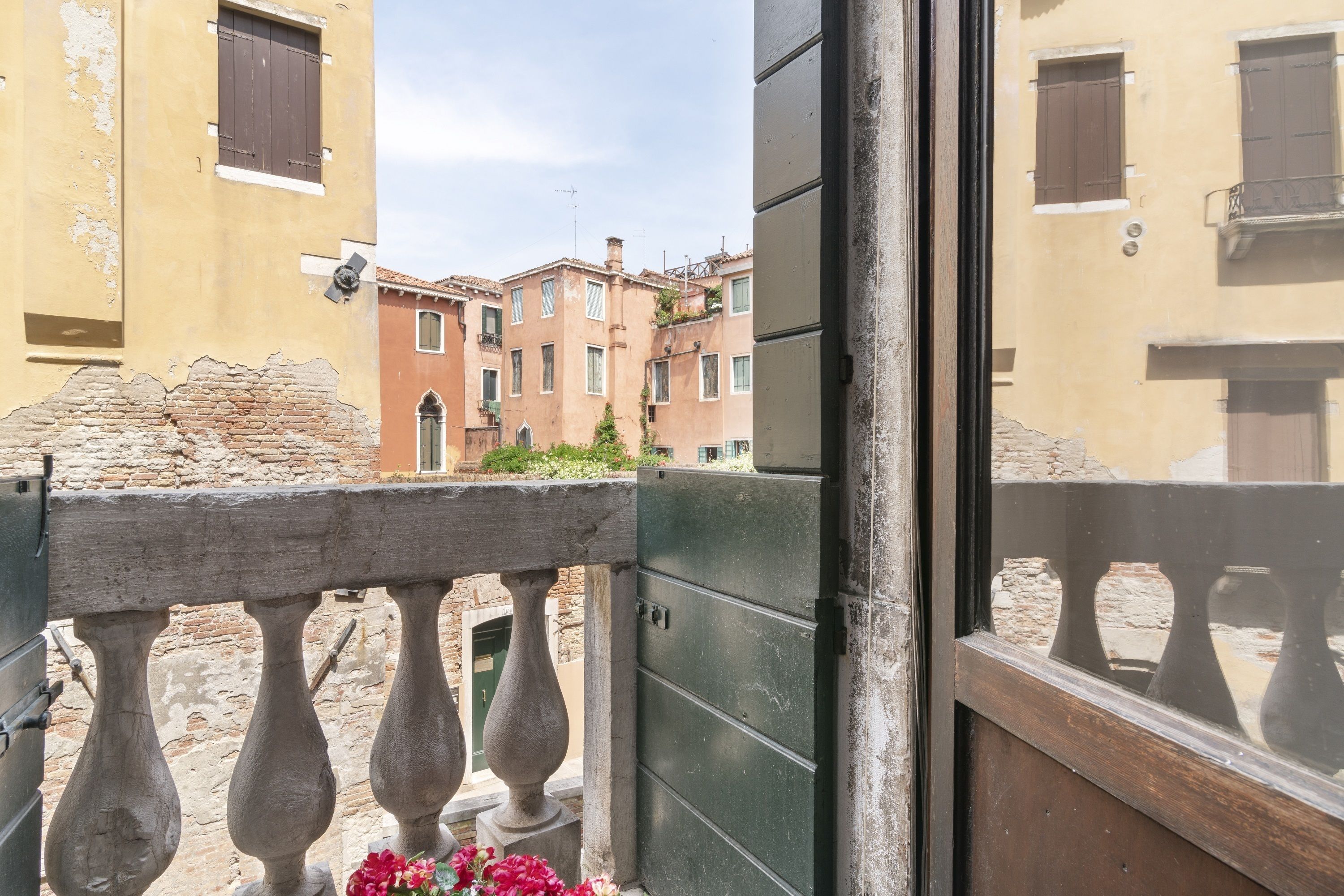 A balcony with a wrought iron railing, a stone wall, and a view of neighboring buildings with traditional architecture.