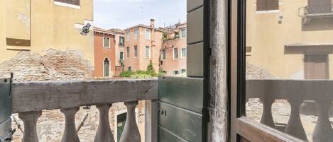 A balcony with a wrought iron railing, a stone wall, and a view of neighboring buildings with traditional architecture.