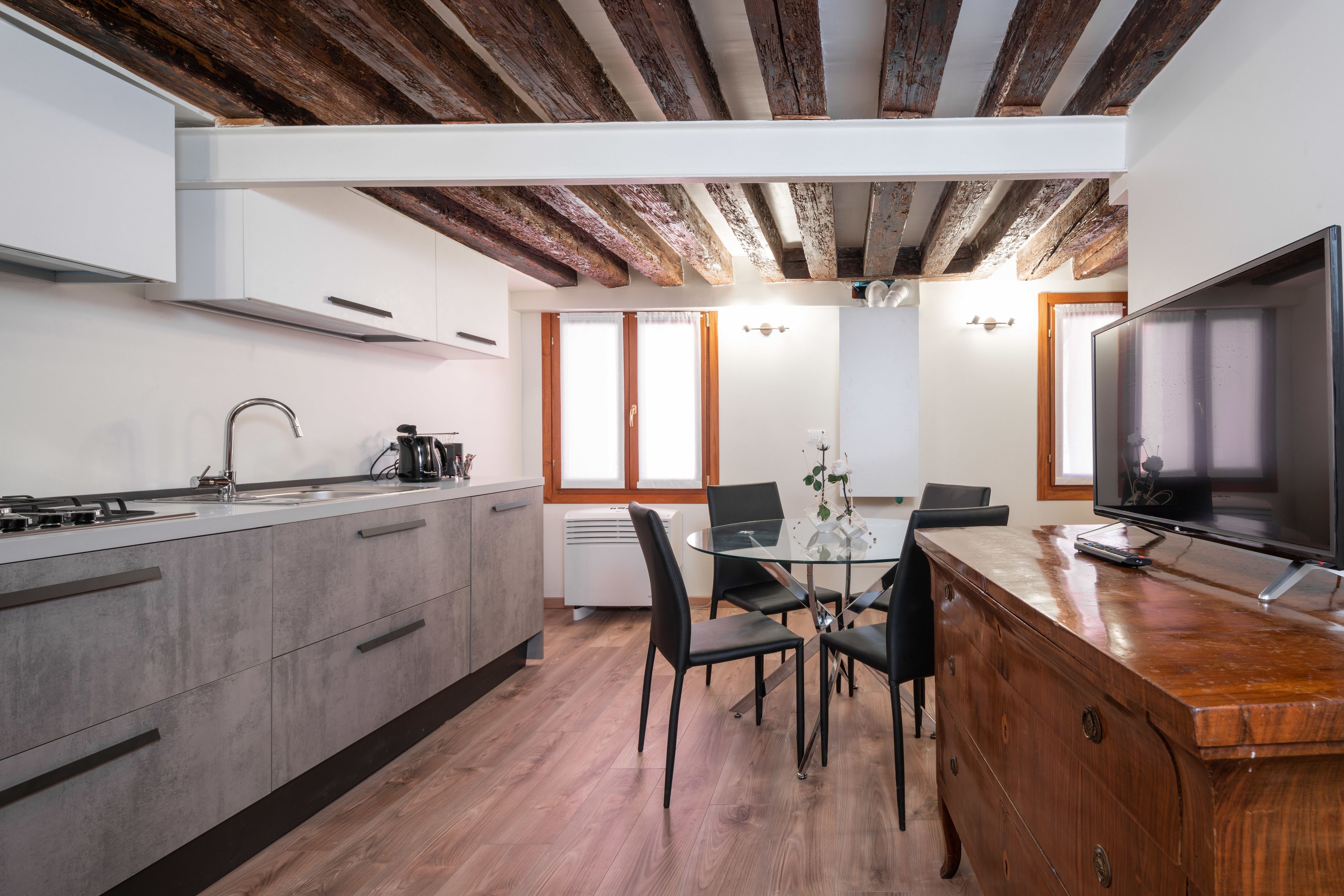 Une cuisine moderne avec un coin repas, des poutres apparentes en bois au plafond et un grand téléviseur.