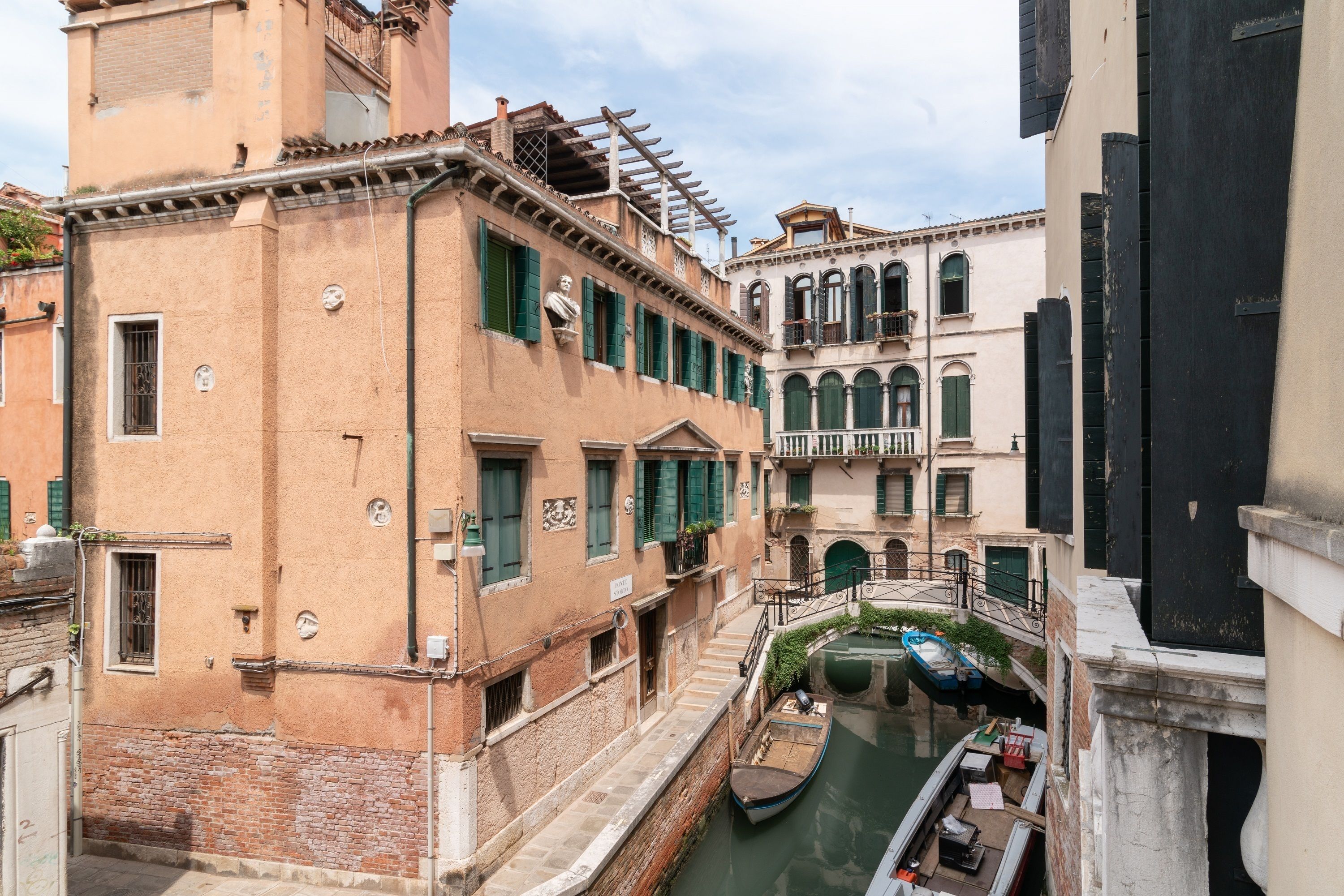 Un canal estrecho con una barca amarrada a la derecha, rodeado de edificios históricos con arquitectura tradicional y contraventanas verdes.