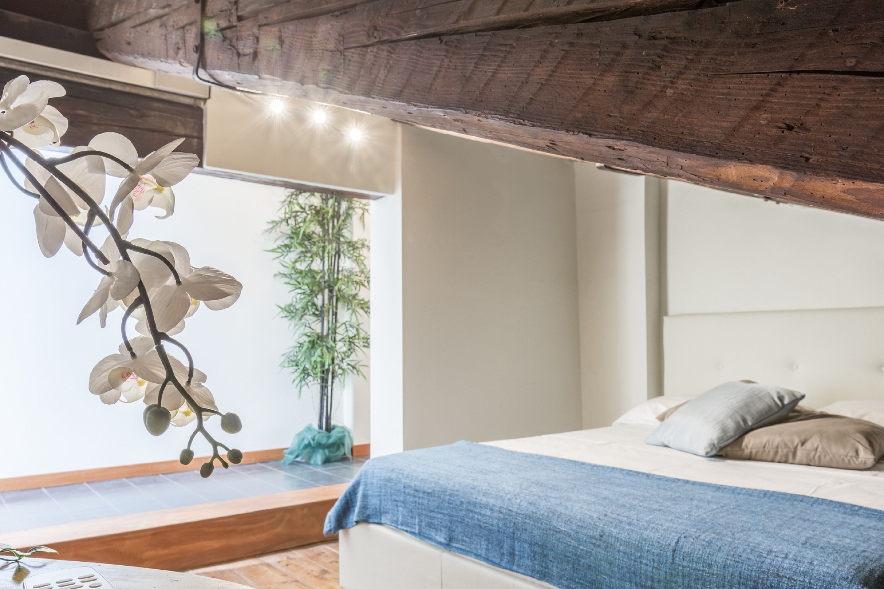 A bedroom with a bed, pillows, a blue blanket, a wooden ceiling, and an orchid plant.