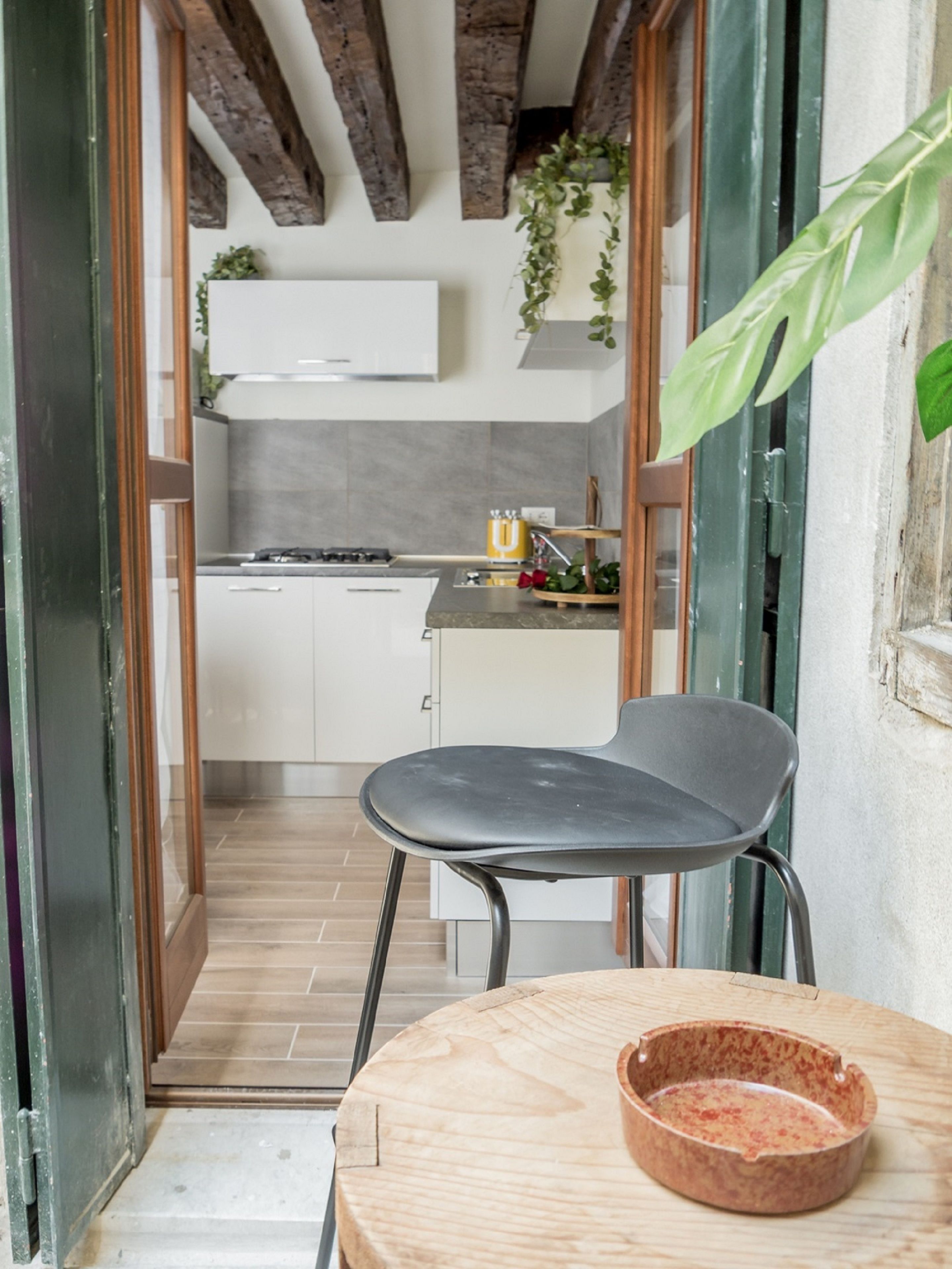 Cocina moderna con armarios blancos, encimera gris y una silla de madera junto a una mesa redonda con un cuenco.