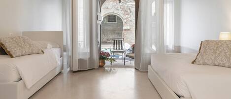A bedroom with two beds, a view of an outdoor patio, and a stone archway.