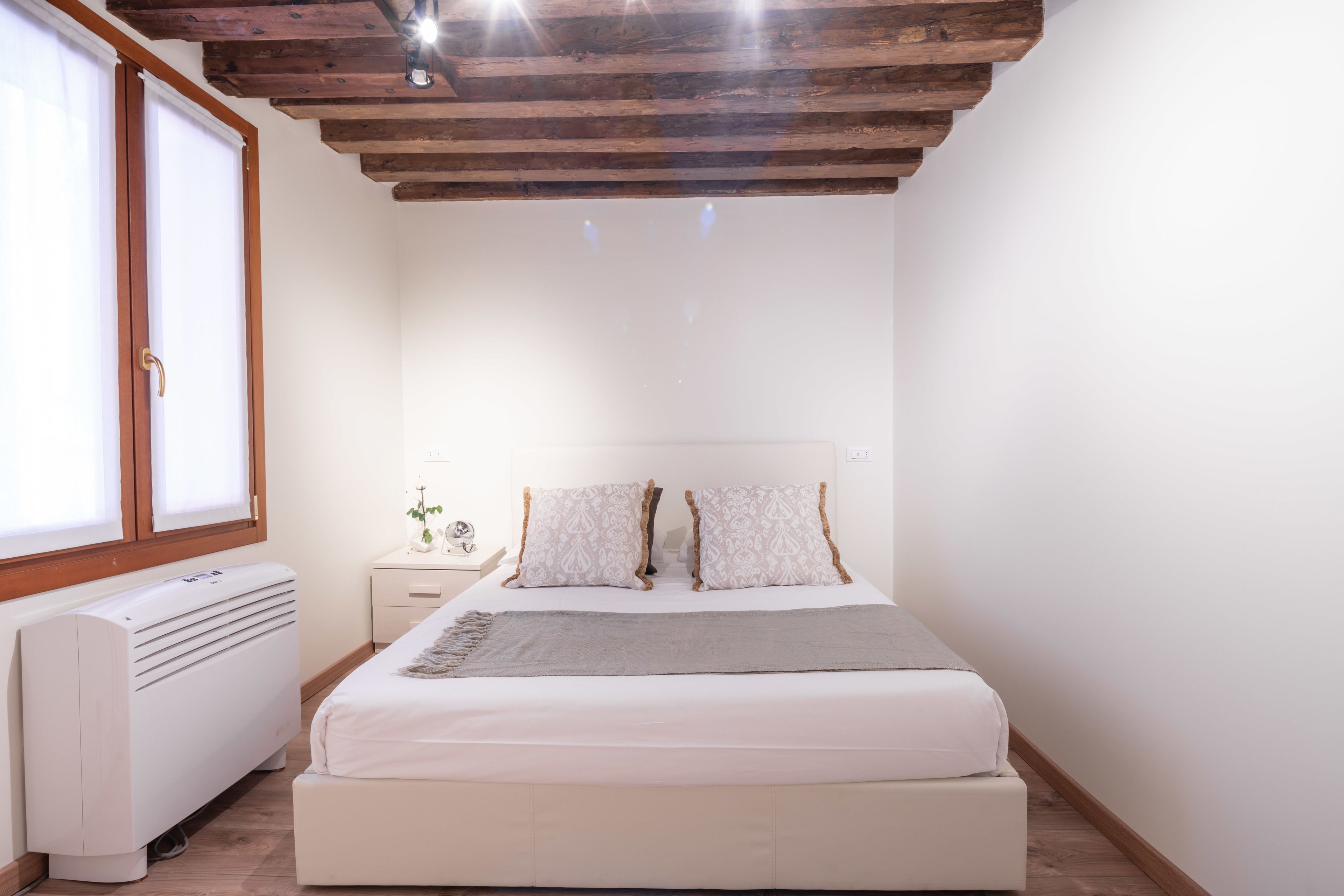 A bedroom with a bed, a nightstand, a heater, and a window.