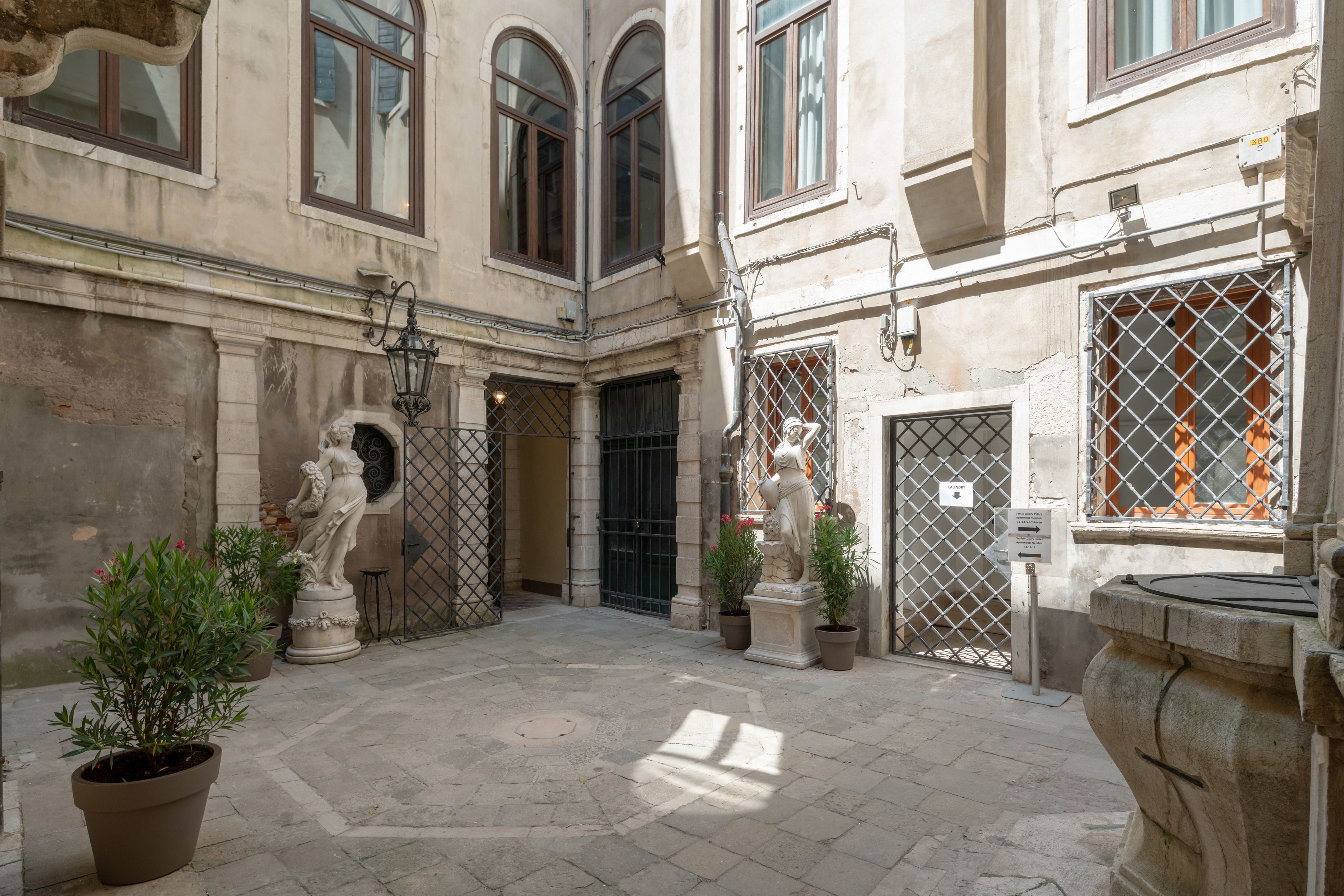 Une cour dallée de pierres, agrémentée de plantes en pot et de statues classiques.