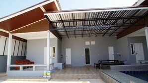 A covered outdoor area with a pool, seating, and a door leading to the house. - Baan Samart 2 Pool Villa Hua Hin (Hua Hin)