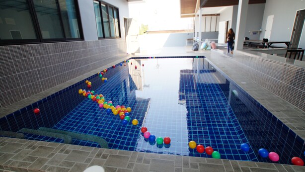 A swimming pool with colorful balls, tiled walls, and a covered seating area. - Baan Samart 2 Pool Villa Hua Hin (Hua Hin)