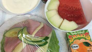 Un refrigerador con varios alimentos, incluyendo una sandía, un plátano, un tazón de cereal, un envase de yogur, un paquete de queso y una caja de jugo de naranja.