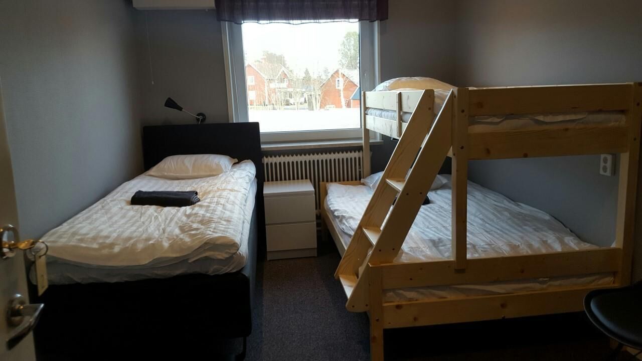 A small room with two beds, one with a headboard and one with a bunk. There is a window with a view of buildings outside.