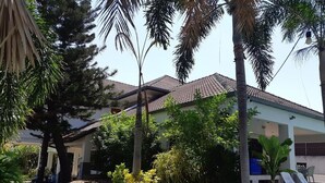 A residential area with a house featuring a tiled roof, surrounded by lush greenery including palm trees and various plants. - Baan Sudrak Pool Villa Hua Hin (Hua Hin)