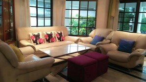A living room with a beige sofa set, a coffee table, and a view of greenery outside. - Baan Sudrak Pool Villa Hua Hin (Hua Hin)