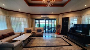 A spacious living room with a large TV, comfortable seating, and a decorative chandelier. - Baan Sudrak Pool Villa Hua Hin (Hua Hin)