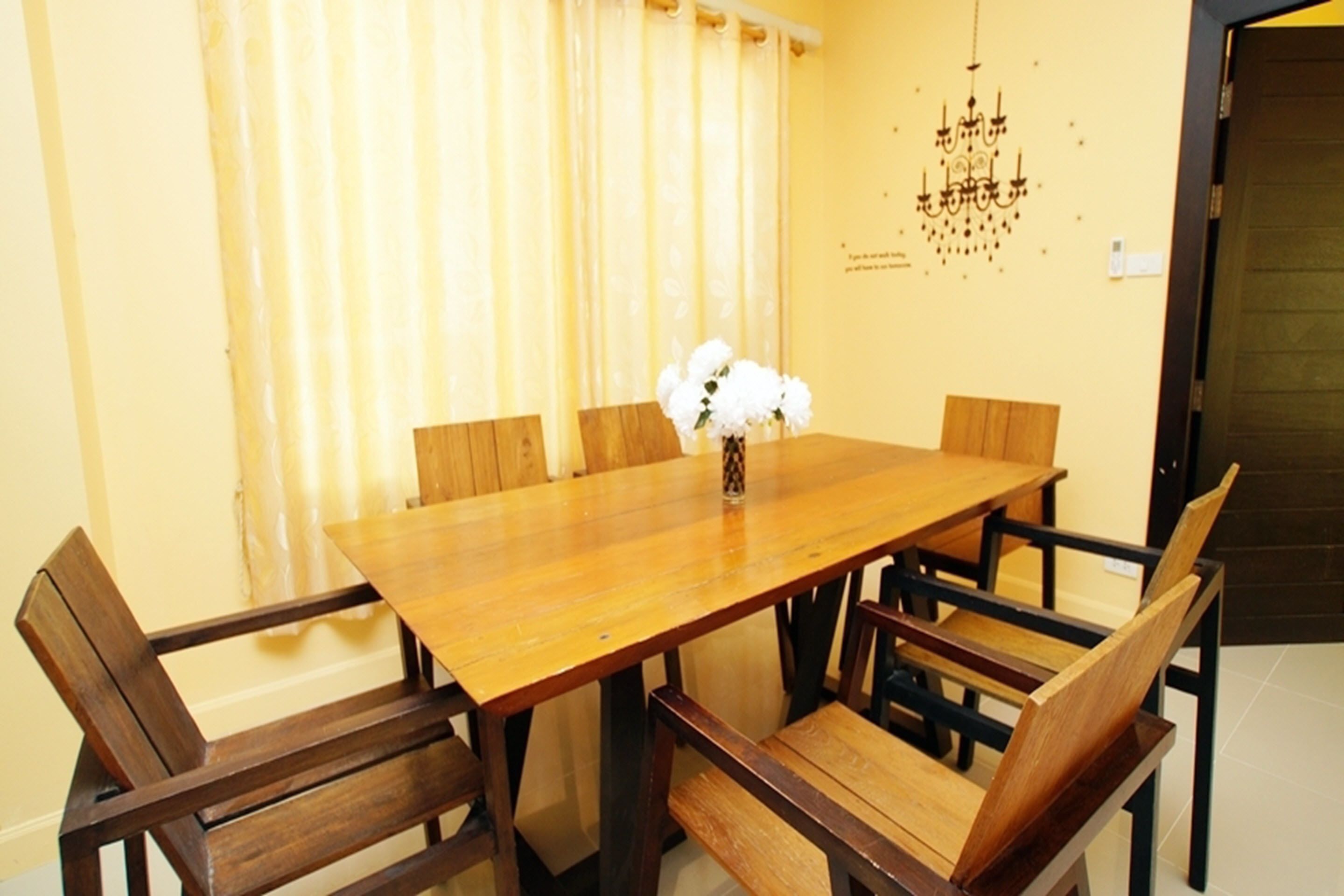 A dining area with a wooden table and chairs, a vase with white flowers, and a chandelier on the wall.
