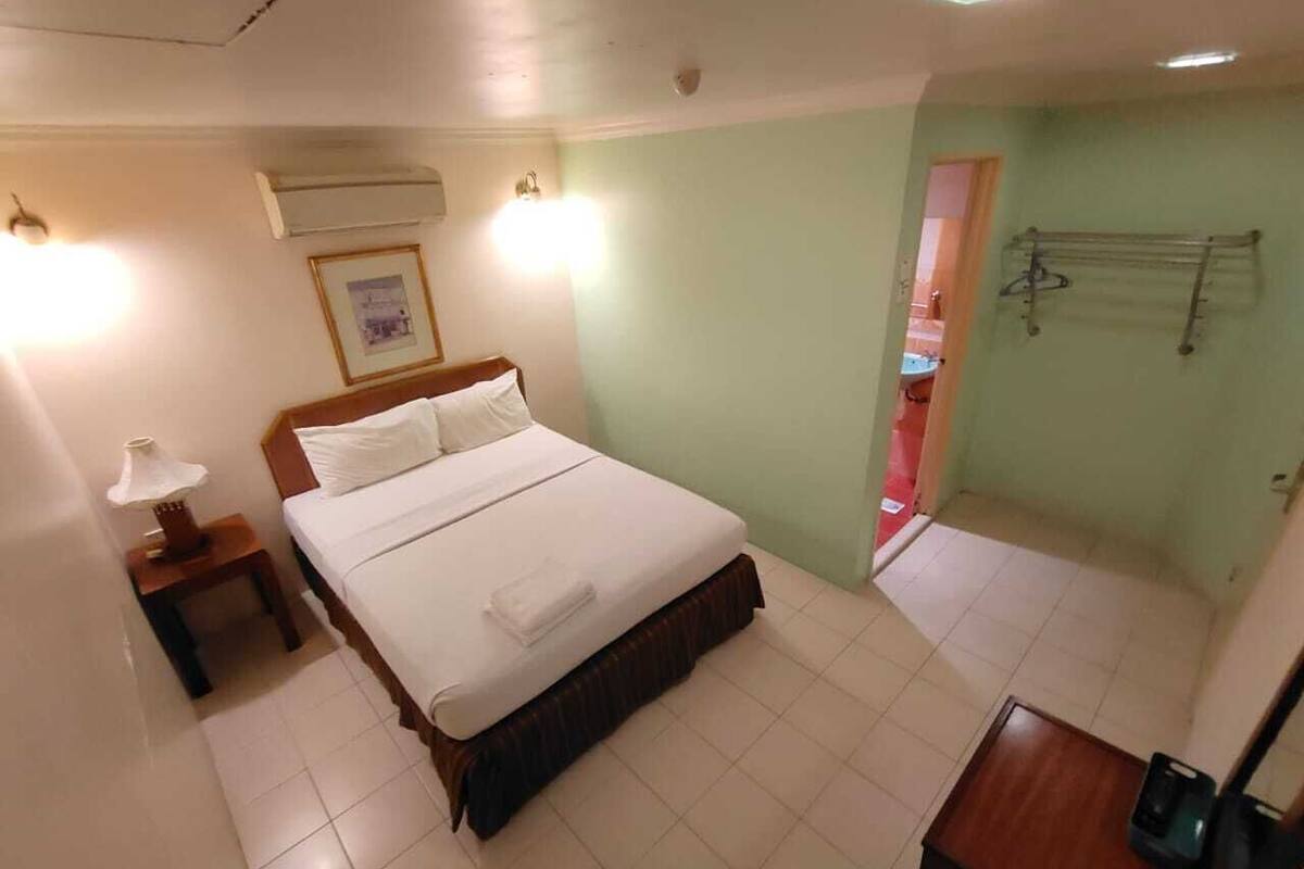 Una habitación de hotel con cama, mesita de noche, lámpara, un cuadro enmarcado y una puerta que da a otra habitación.