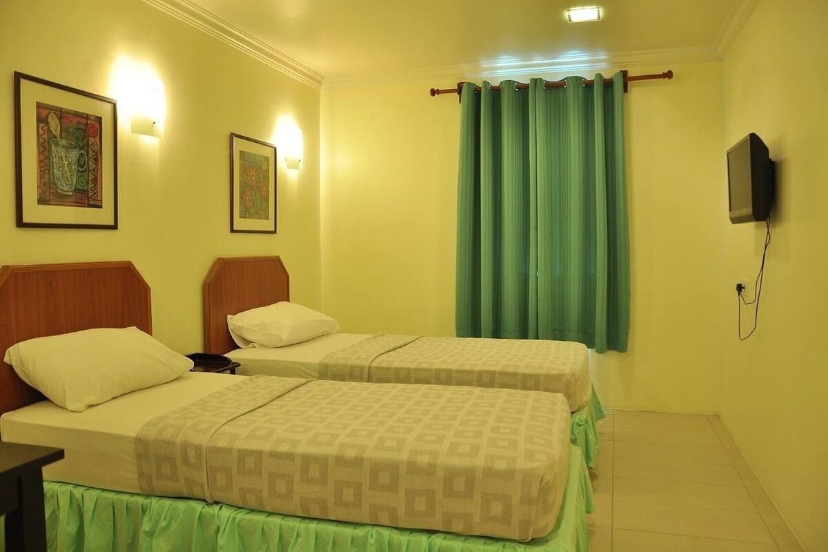Habitación de hotel con dos camas, una cortina verde y obras de arte colgadas en la pared.