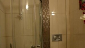 A bathroom with a glass-enclosed shower, a toilet, and a trash bin. - Manolya Hotel (Bodrum)