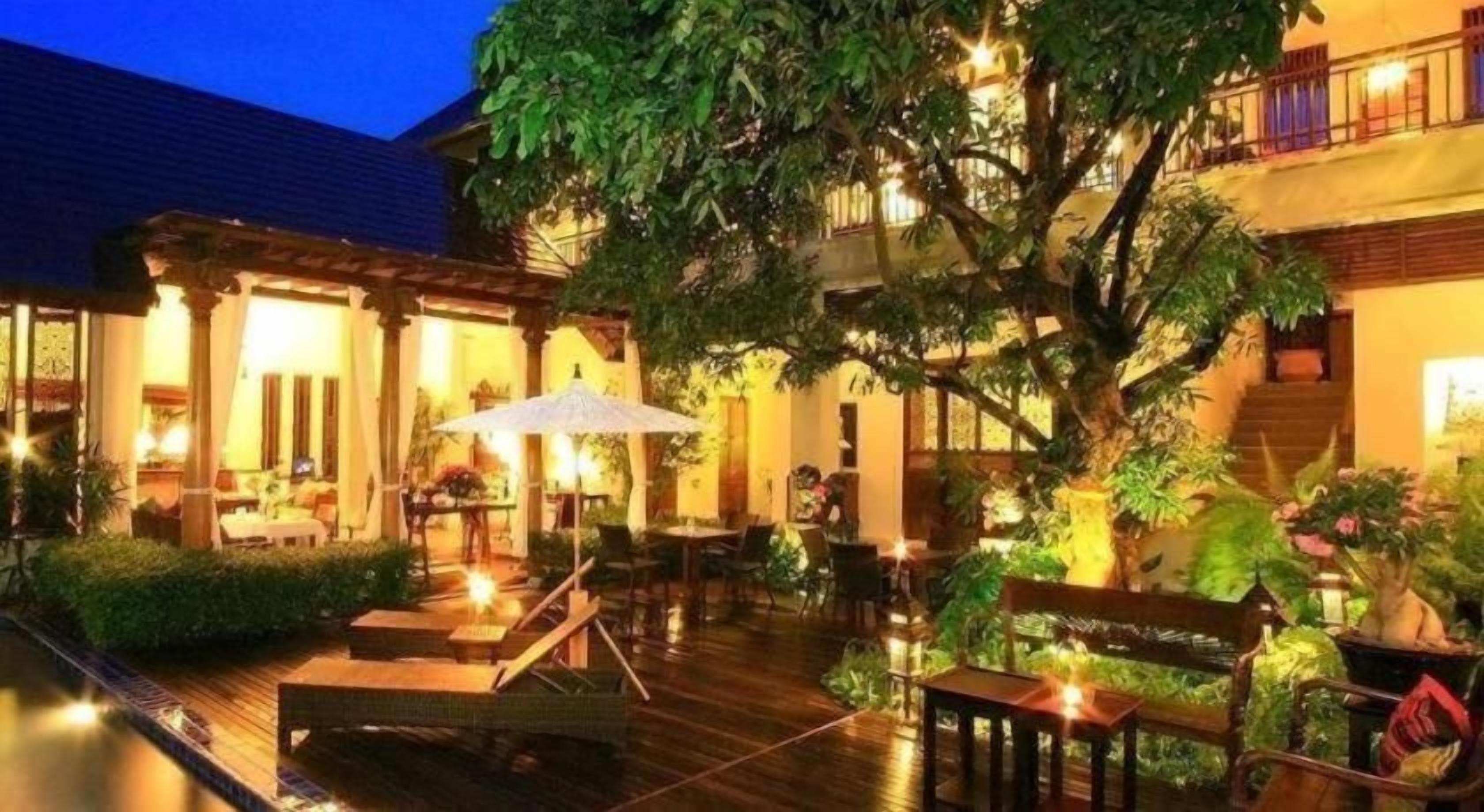 An outdoor seating area with tables and chairs, surrounded by greenery and a pool.